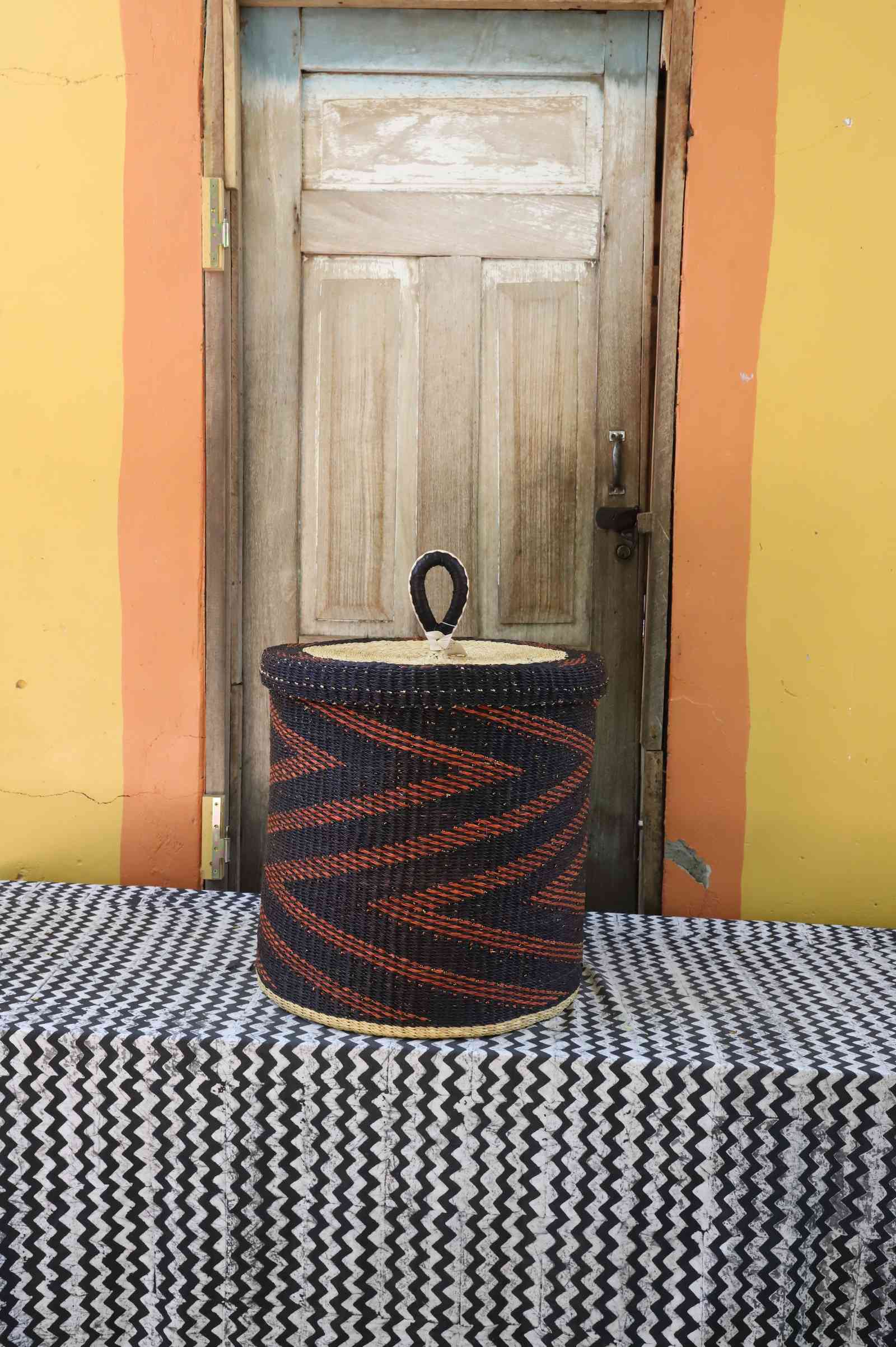 Handwoven Bolga laundry basket with lid in dark blue with a rust-orange zigzag arrow pattern.