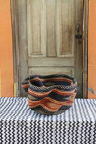 Handwoven Bolga wave basket with a fluted rim in natural straw with black and orange wave stripes.