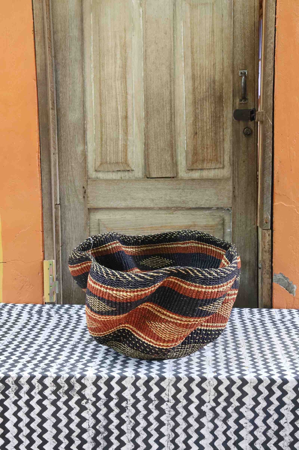 Handwoven Bolga wave basket with a fluted rim in natural straw with black and orange wave stripes.