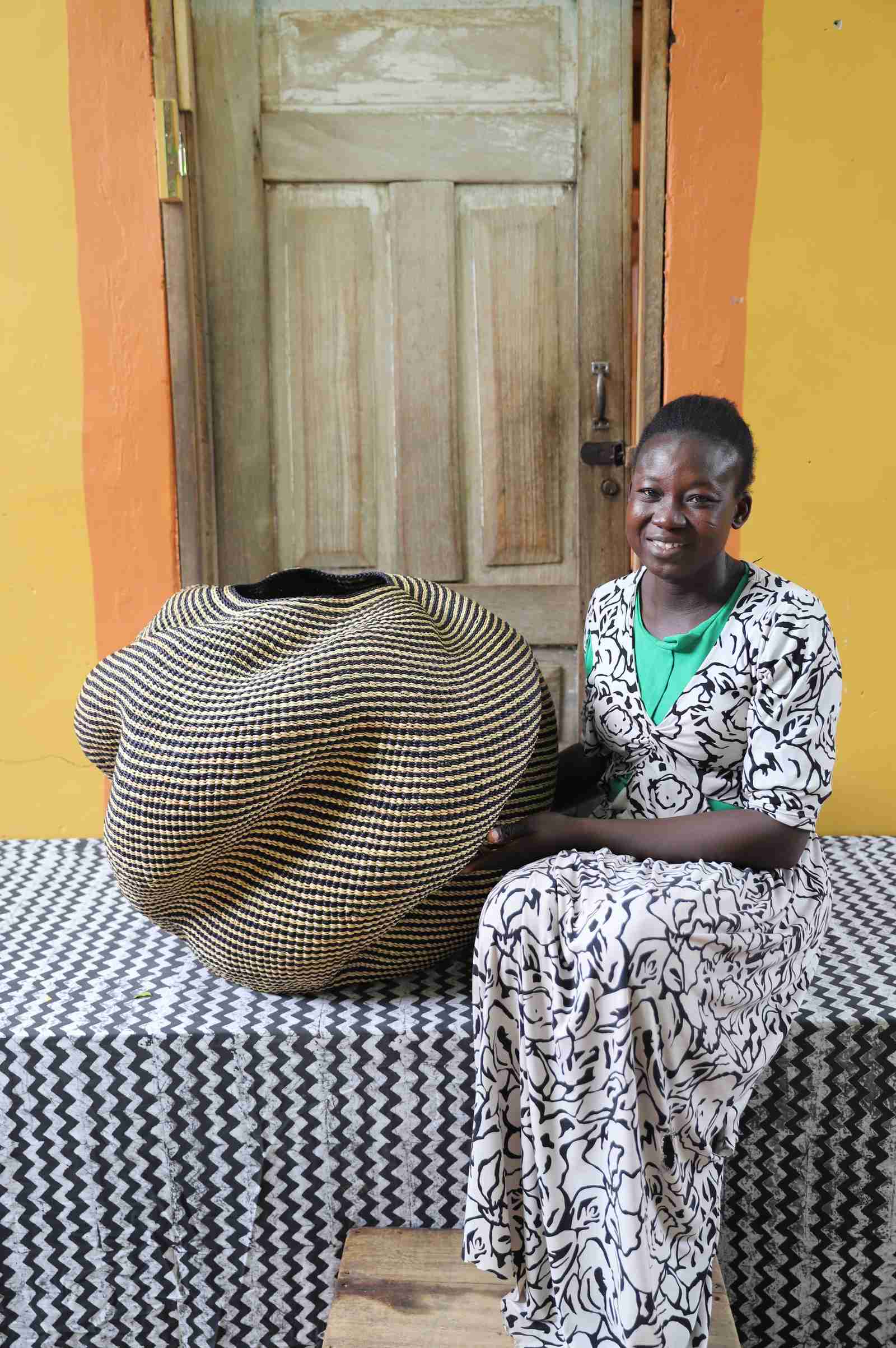 Large nest-shaped Bolga art basket in natural straw, shown beside a seated person for scale.