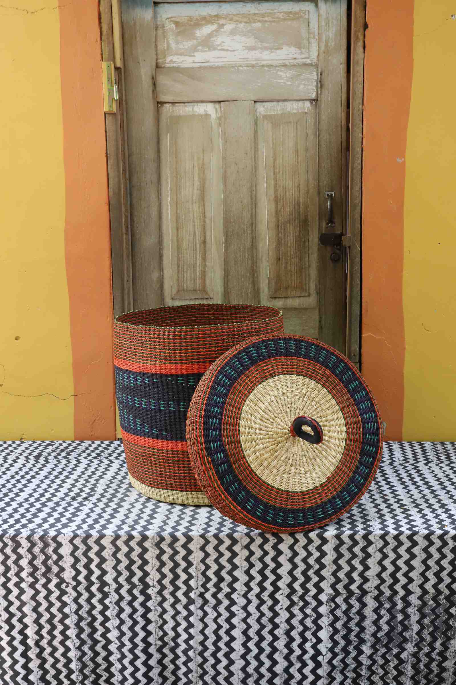 Large Bolga laundry basket with lid removed, rust-orange body with dark banded accent and matching lid.