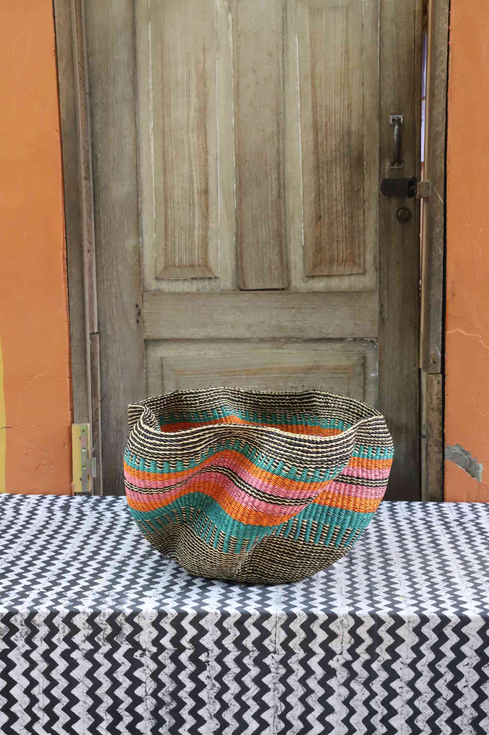 Handwoven Bolga wave basket in natural straw with fine teal, orange and black wavy horizontal stripes.
