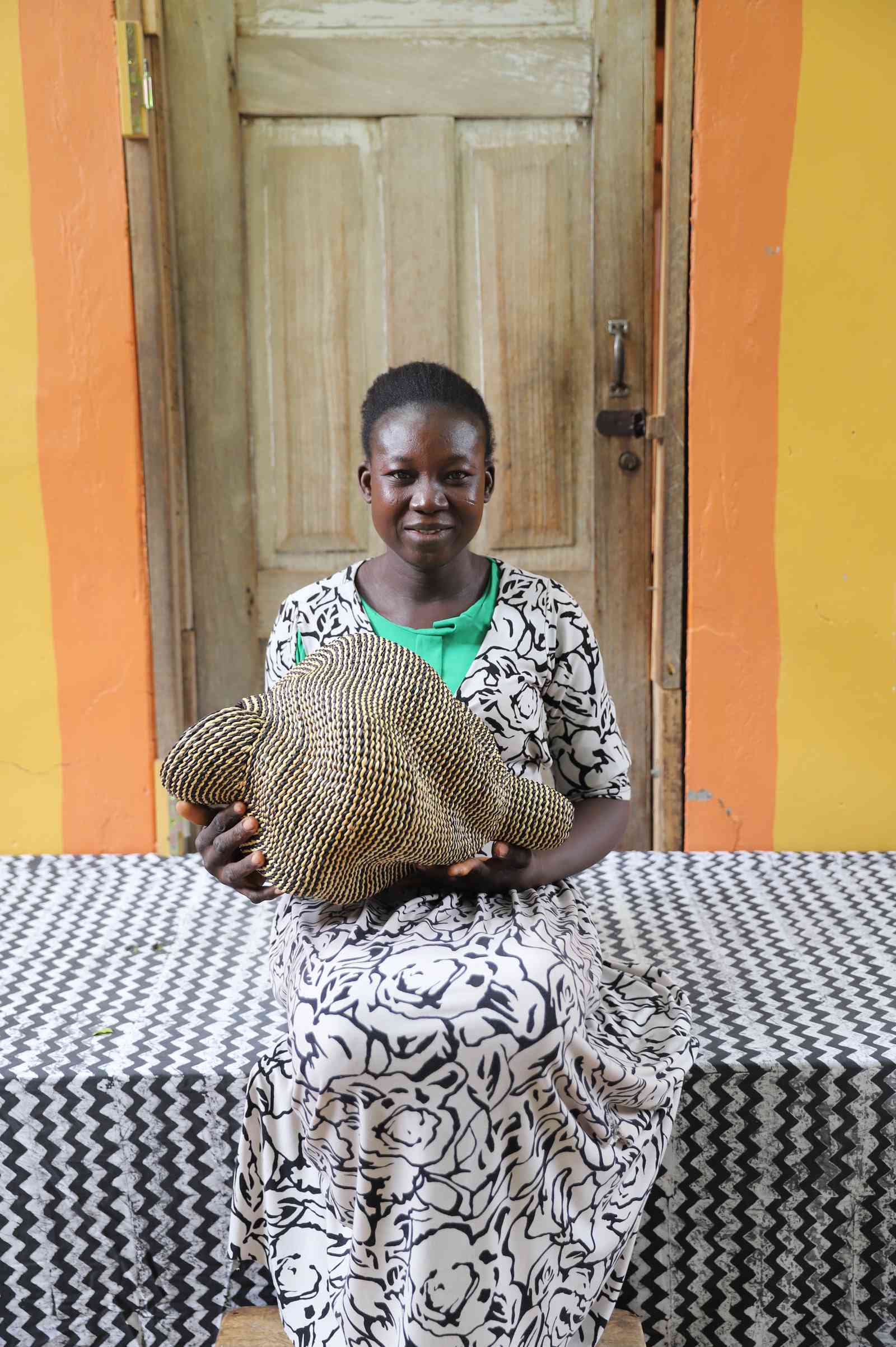 Small spiral-form Bolga art basket in natural straw, held by a seated person for scale.
