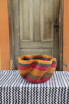 Handwoven Bolga wave basket in natural straw with orange, red and black wavy horizontal stripes.