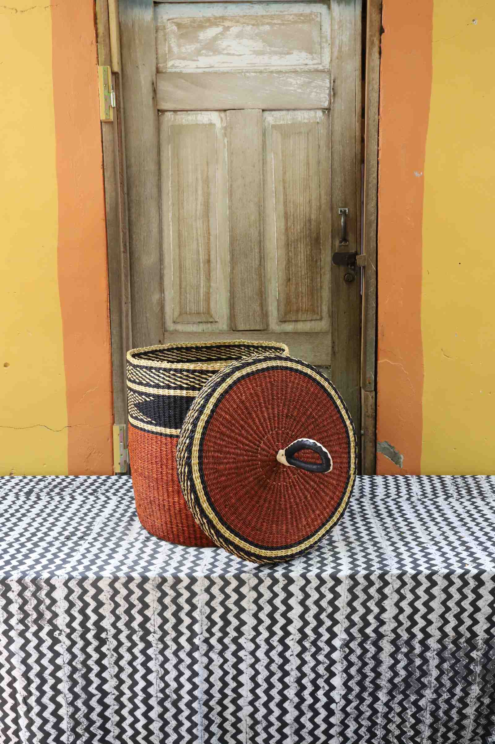 Medium Bolga laundry basket with lid removed, dark top with rust-orange banded base and natural lid interior.