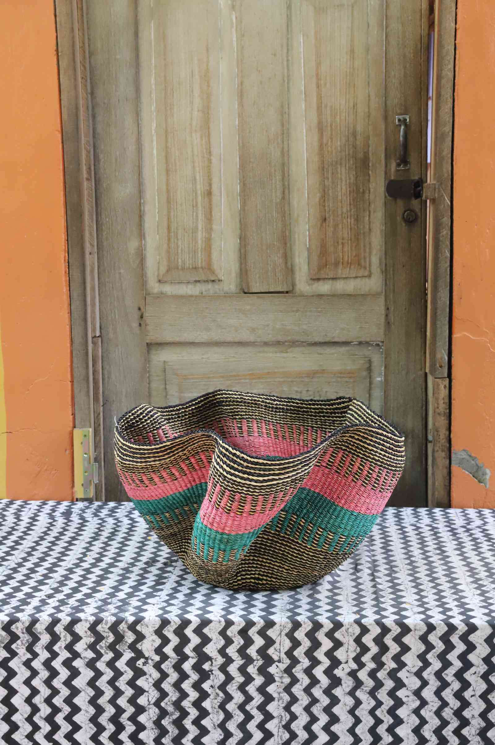 Handwoven Bolga wave basket with a fluted rim in natural straw with pink and teal wave stripes.