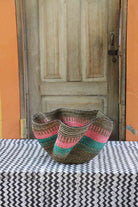 Handwoven Bolga wave basket with a fluted rim in natural straw with pink and teal wave stripes.