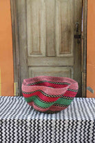 Handwoven Bolga wave basket in natural straw with pink, green and black wavy horizontal stripes.