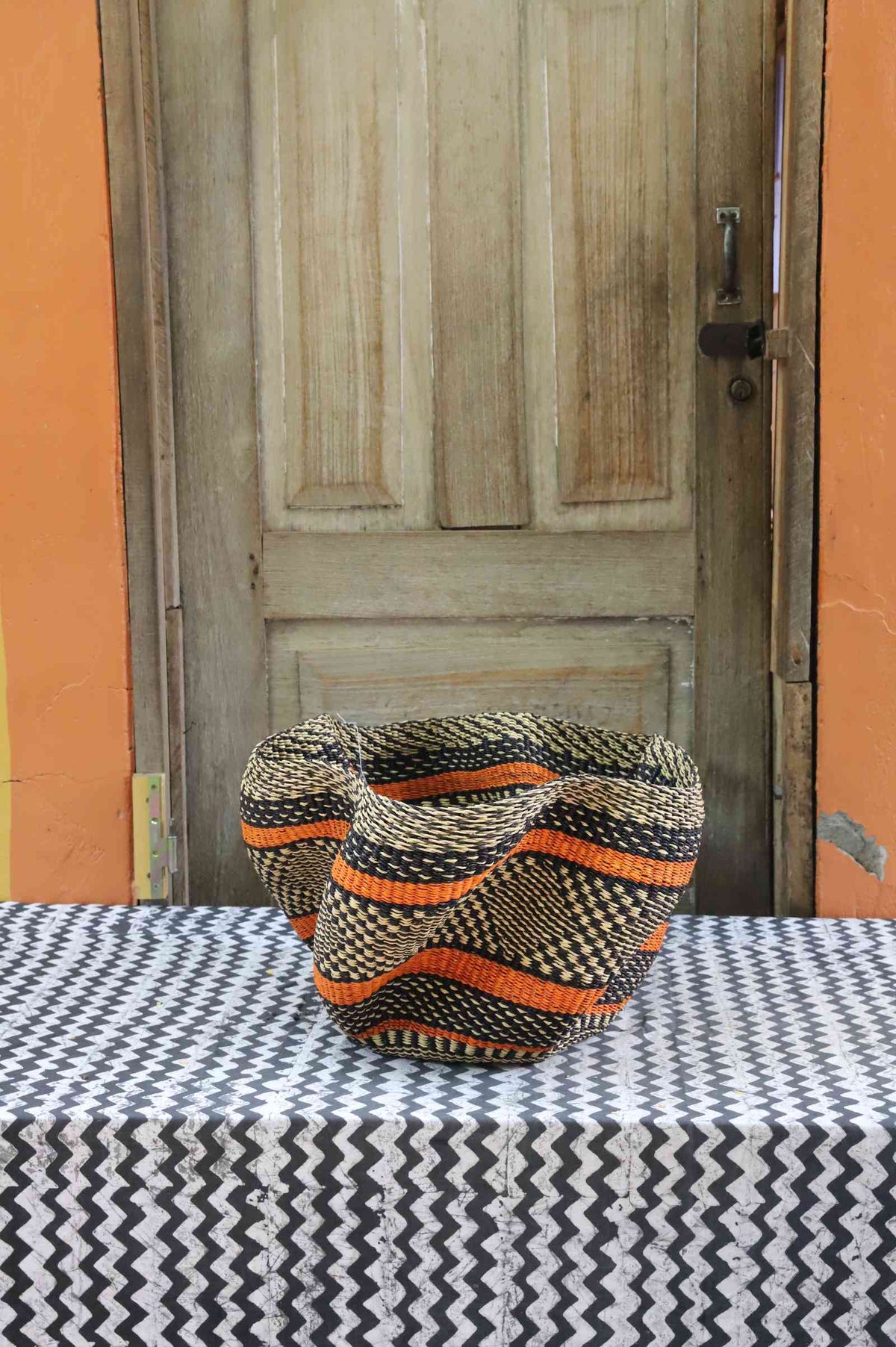 Handwoven Bolga wave basket with a fluted rim in natural straw with bold orange and dark wave stripes.