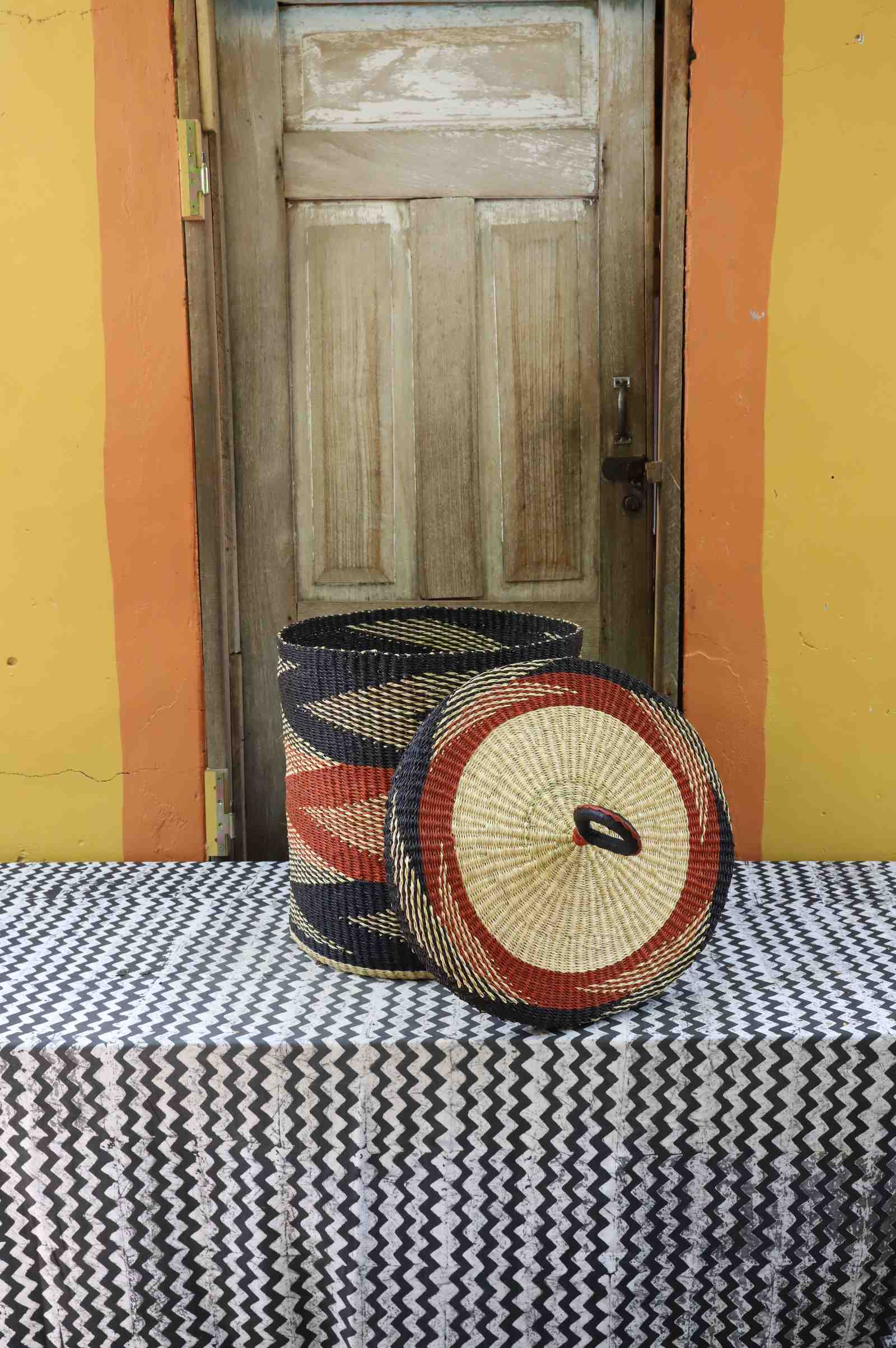Medium Bolga laundry basket with lid removed, natural body with rust-red and black bands and matching lid.