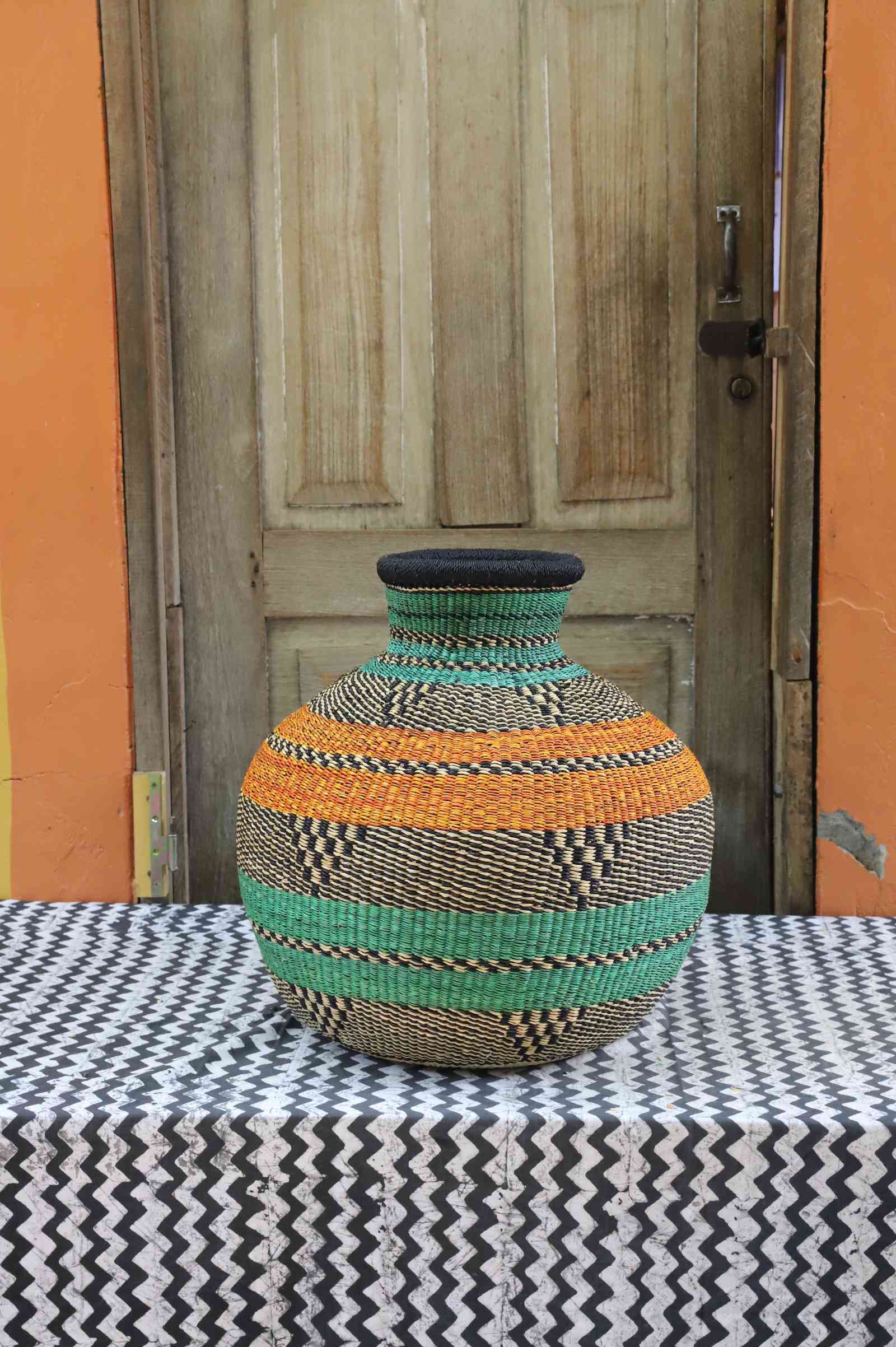 Large handwoven Bolga décor basket in a bulbous pot shape with orange and green bands and black checkered detail.