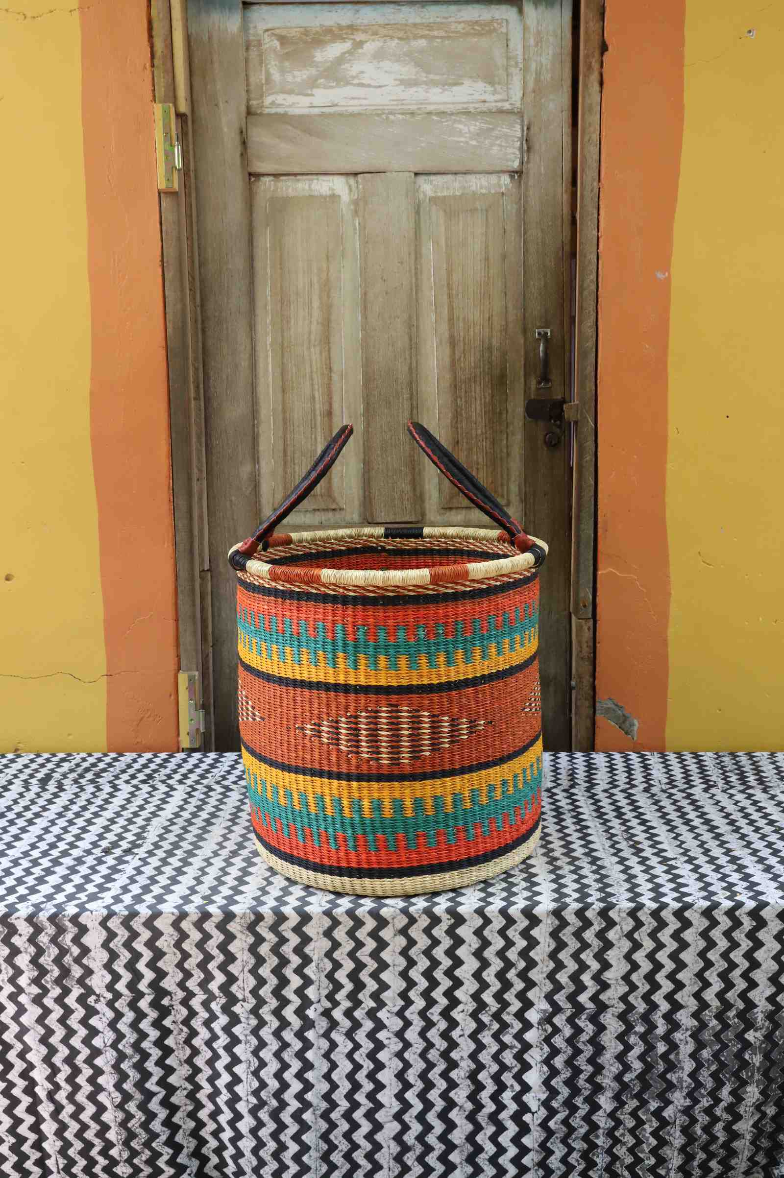 Large handwoven open-top Bolga laundry basket in natural straw with orange, teal and dark banded stripes.