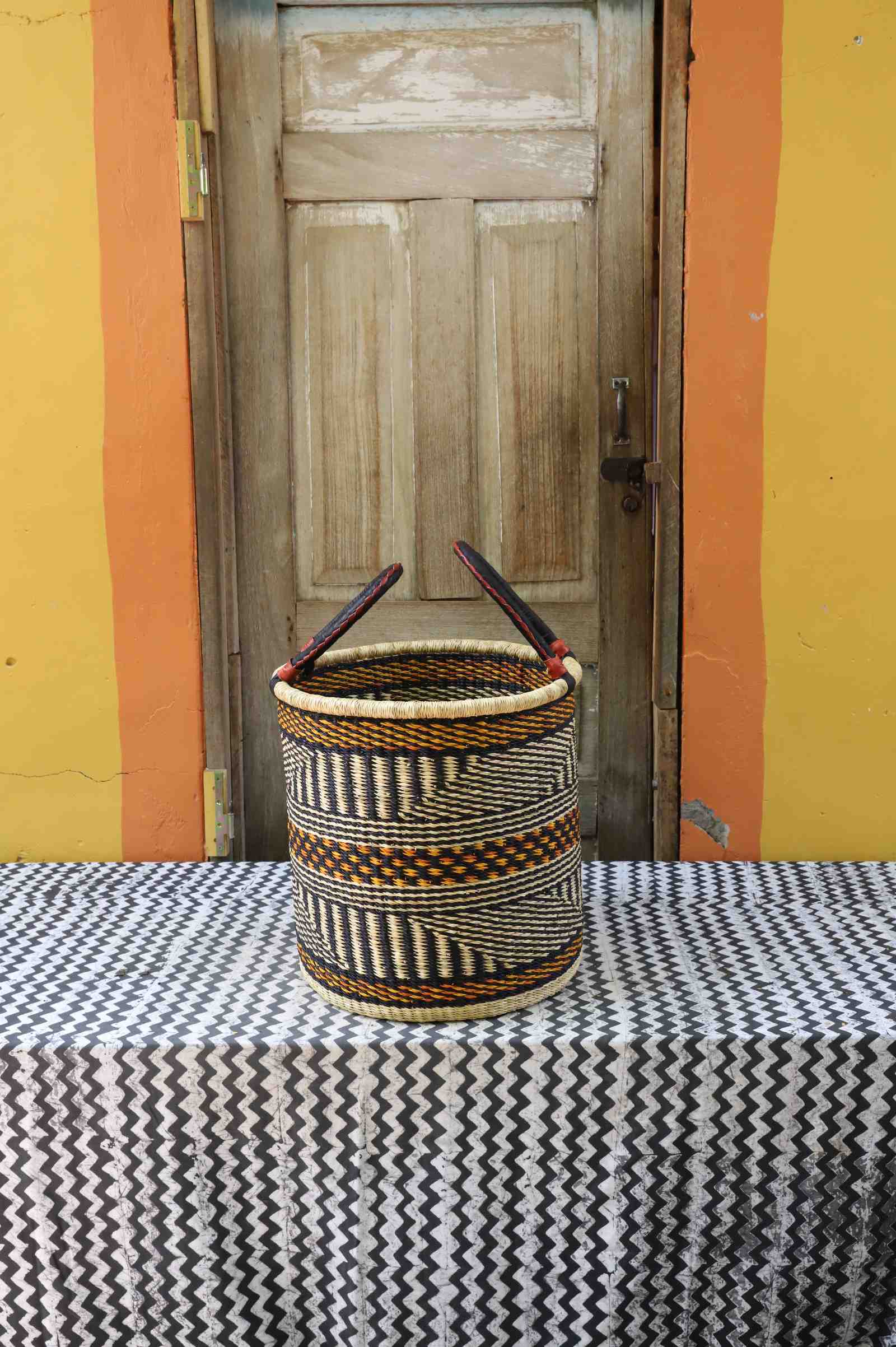 Small handwoven open-top Bolga laundry basket in natural straw with fine dark banded stripes.