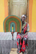 Naba Penga wall fan in green woven straw with an orange border, held by a seated person for scale.