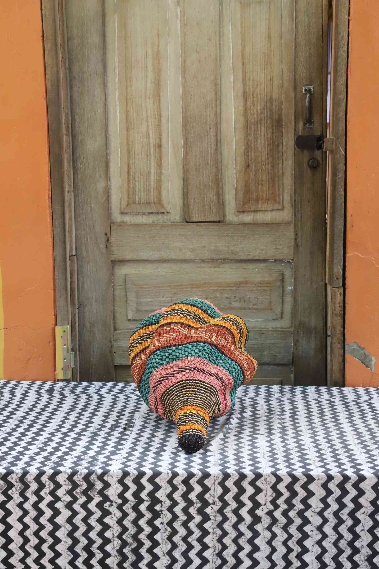 Handwoven Bolga art basket in a conch-shell form, showing the tightly coiled multicolour weave.