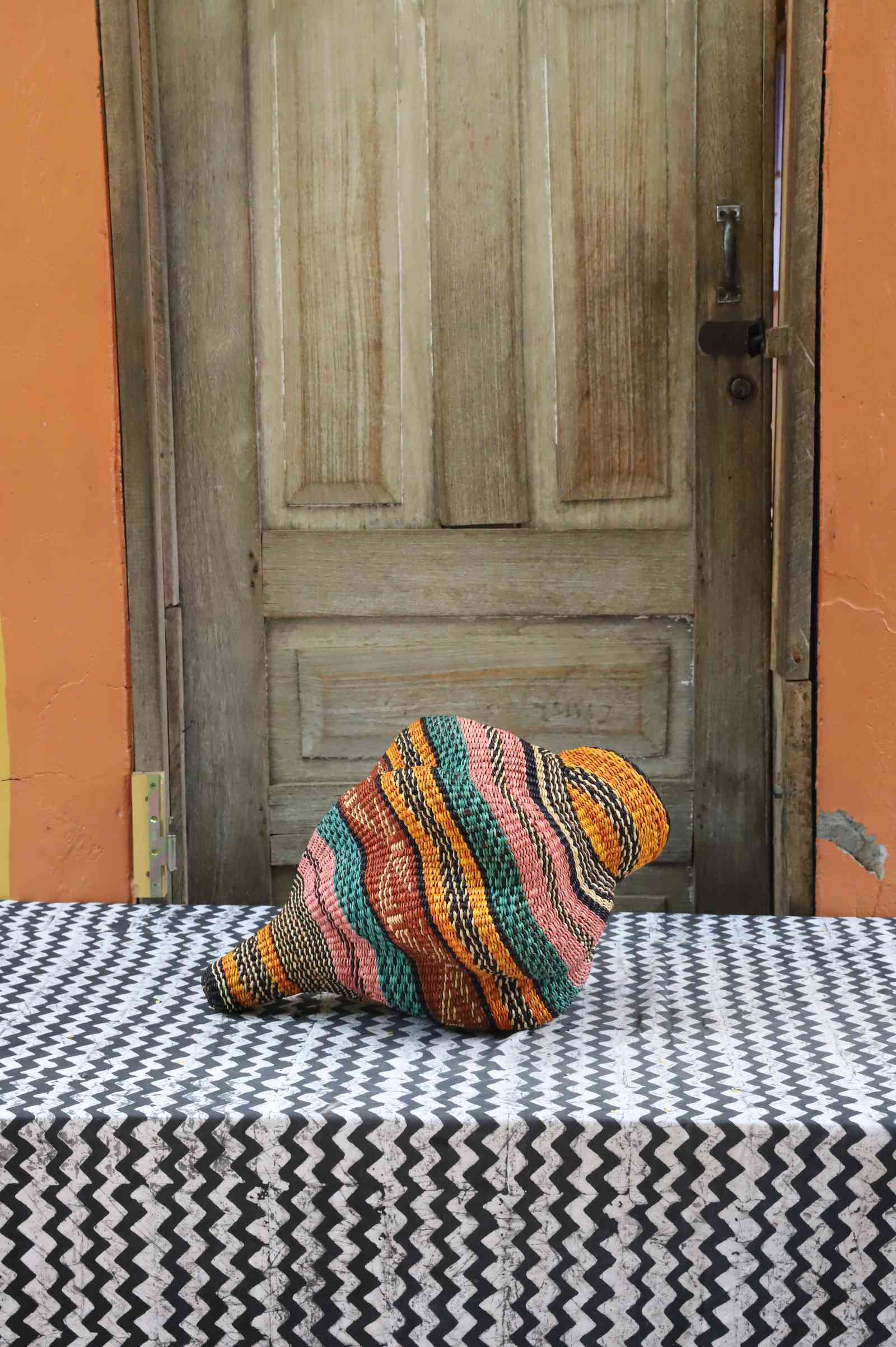 Handwoven Bolga art basket in a curled conch form, side view showing coiled multicolour bands.