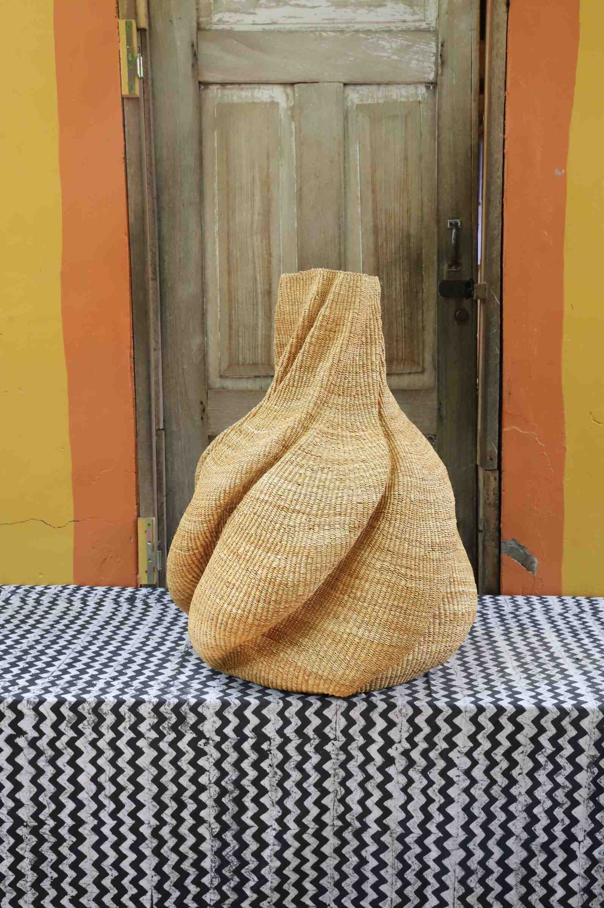 Medium handwoven Bolga art basket in a sculpted natural straw form with pinched and twisted lobes.