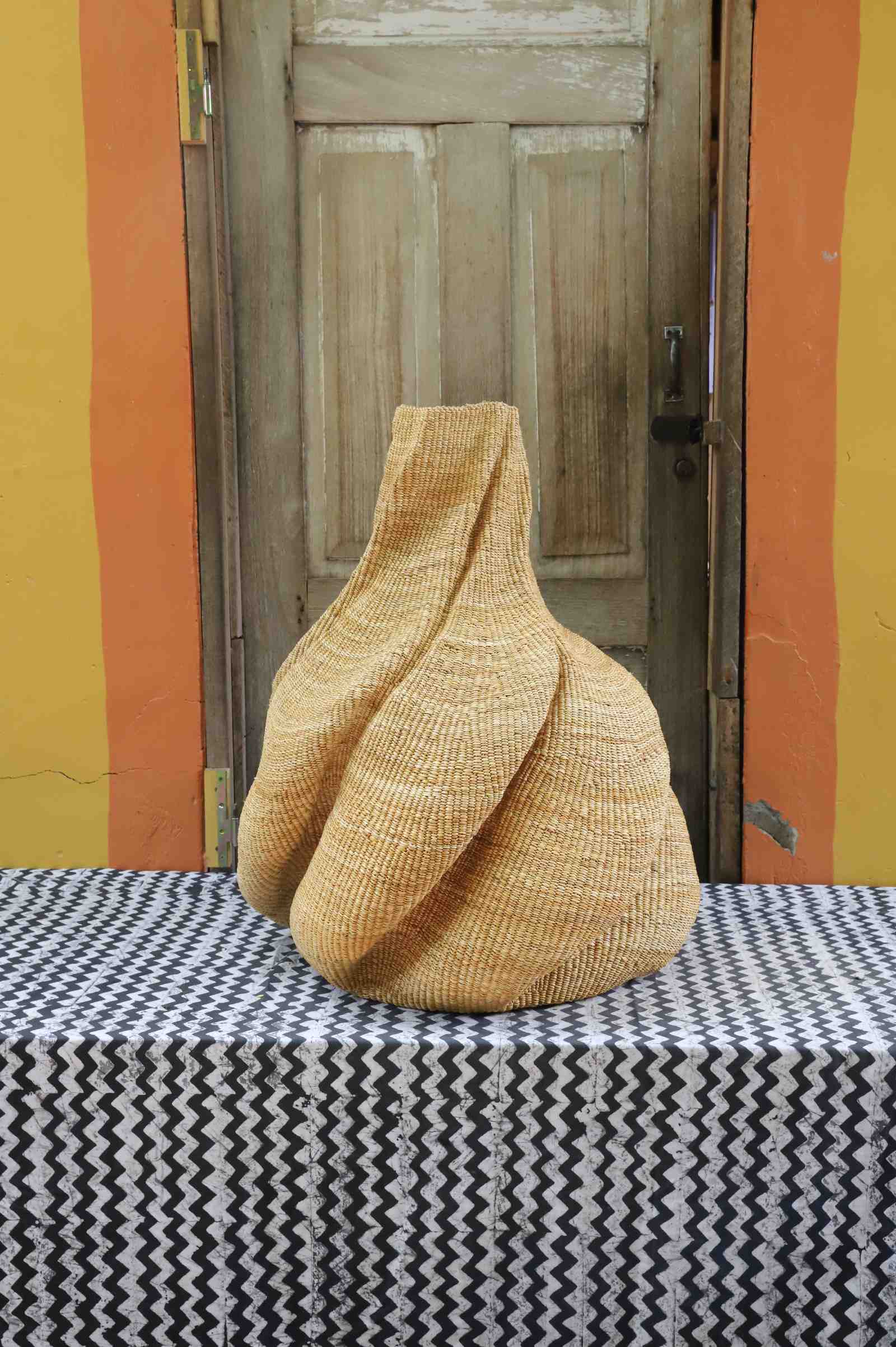 Medium handwoven Bolga art basket in natural straw, side view of the sculpted twisted lobed form.