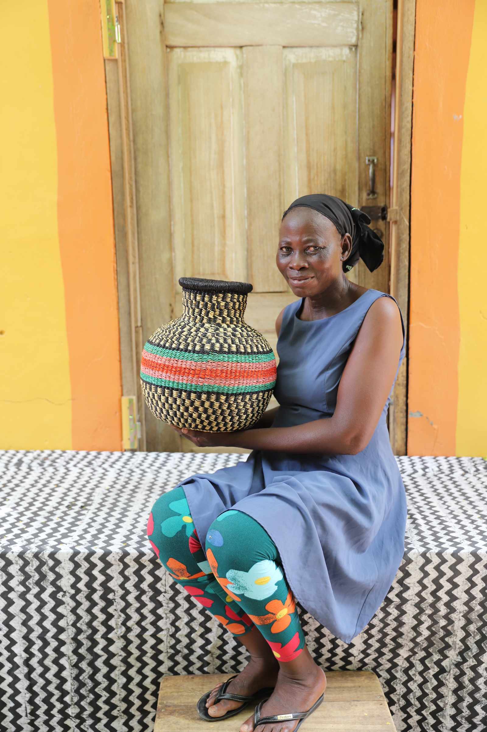 Small vase-shaped Bolga basket with a red and green striped band, held by a seated woman for scale.