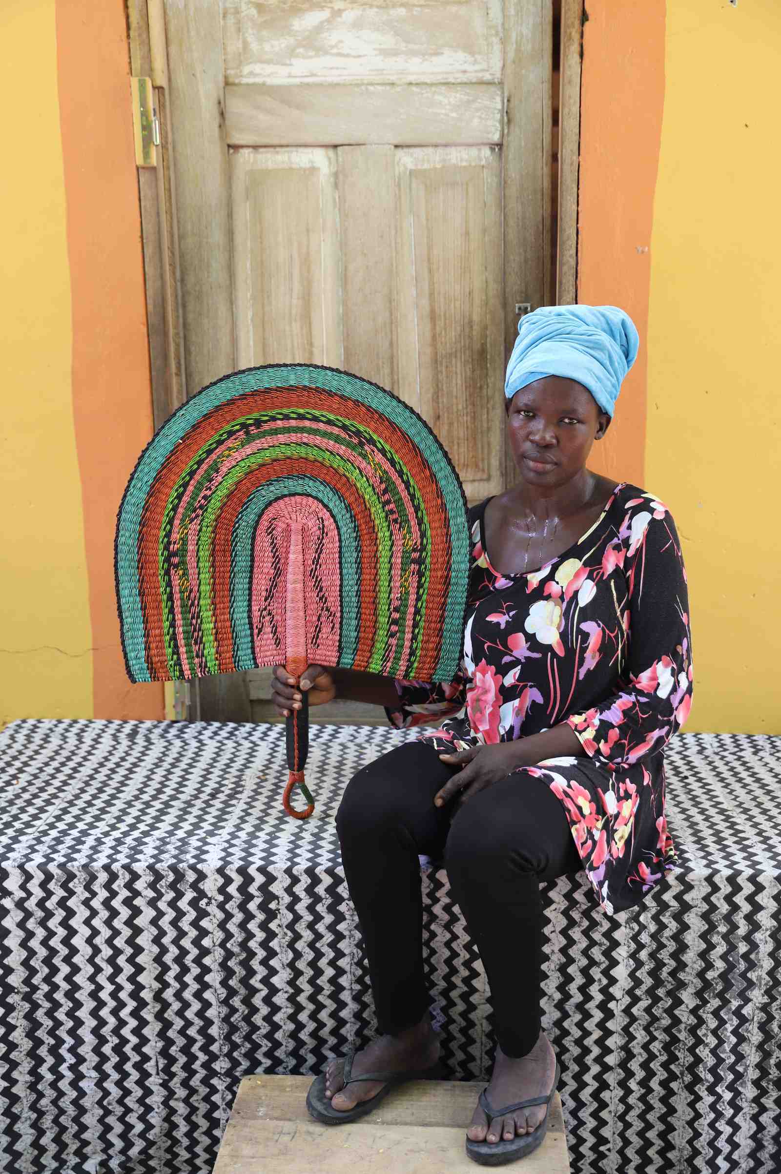 Weaver holding a Naba Penga handwoven wall fan in teal, terracotta and pink, in Bolgatanga, Ghana.