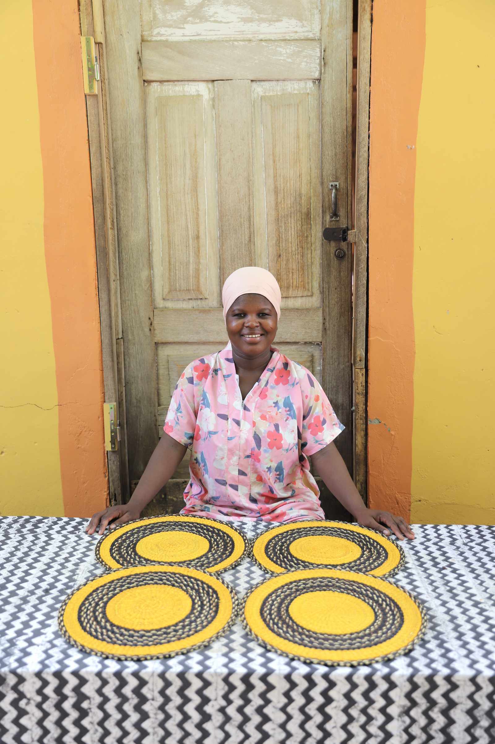 Set of four handwoven Bolga placemats in natural straw with black border rings, displayed by their maker in Ghana.