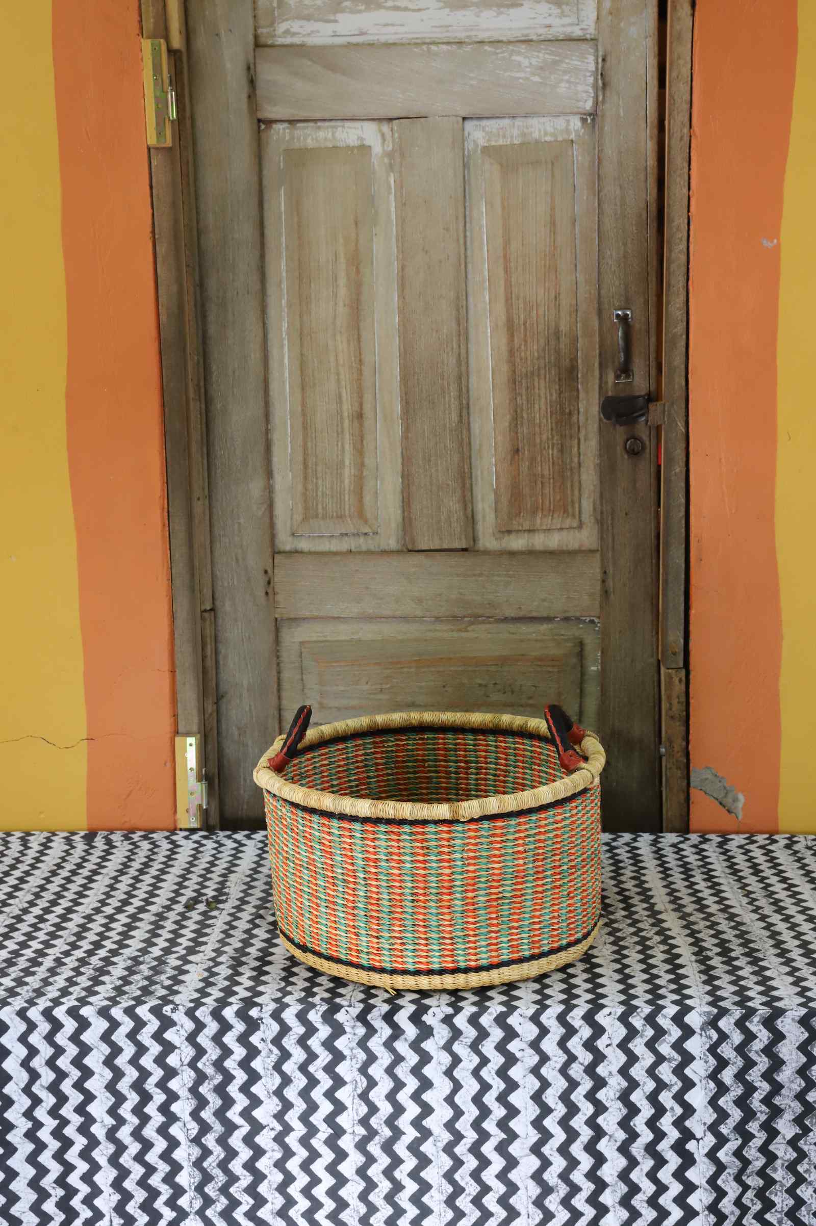 Small handwoven Bolga storage tub in natural straw with orange and green banded stripes.