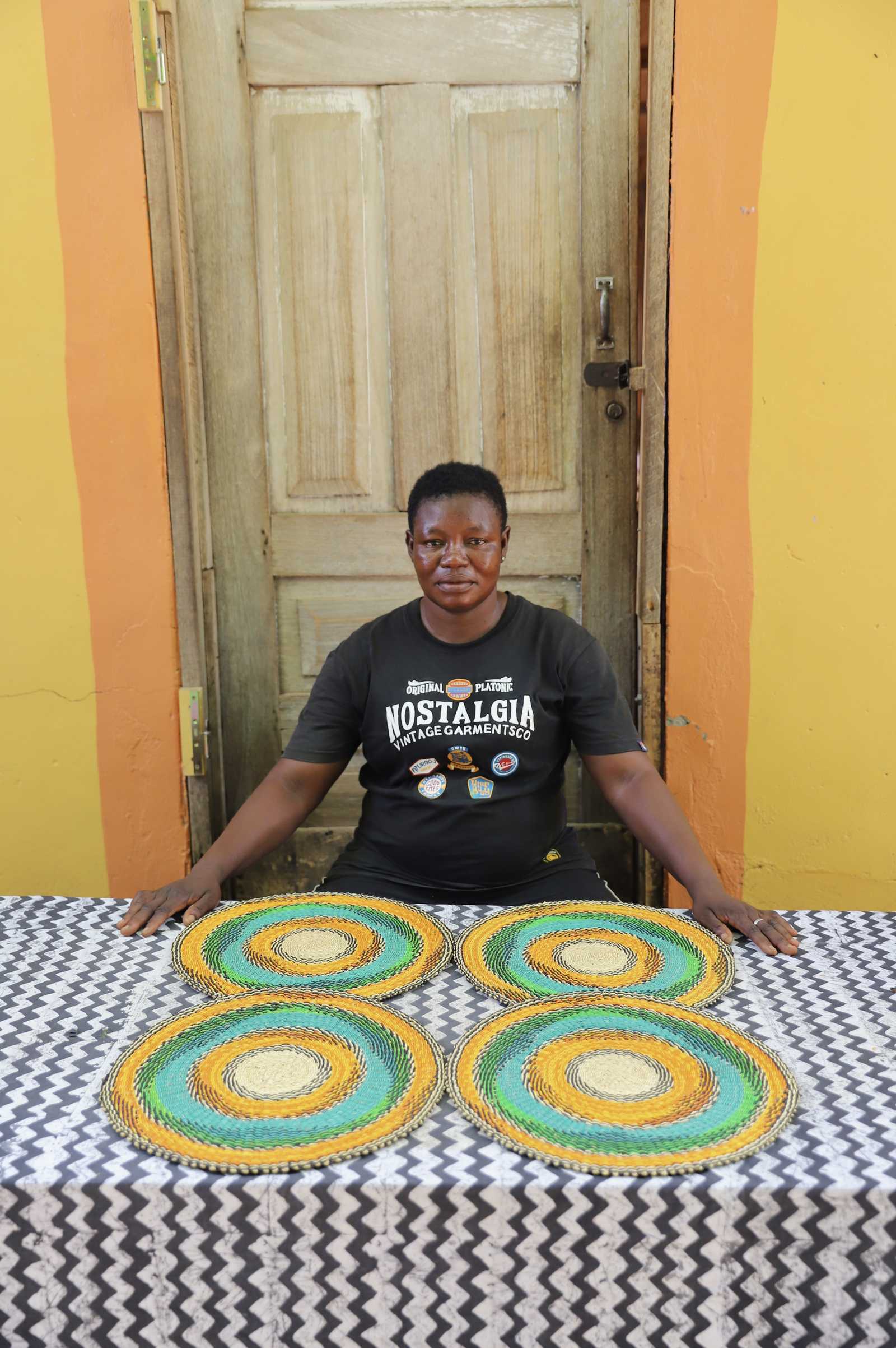 Set of four handwoven Bolga placemats with concentric rings in orange, teal and green, displayed in Ghana.