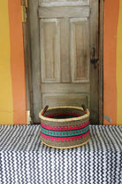 Small handwoven Bolga storage tub in natural straw with red, green and yellow banded stripes.
