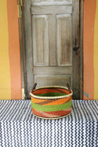 Small handwoven Bolga storage tub in natural straw with fine orange and green banded stripes.