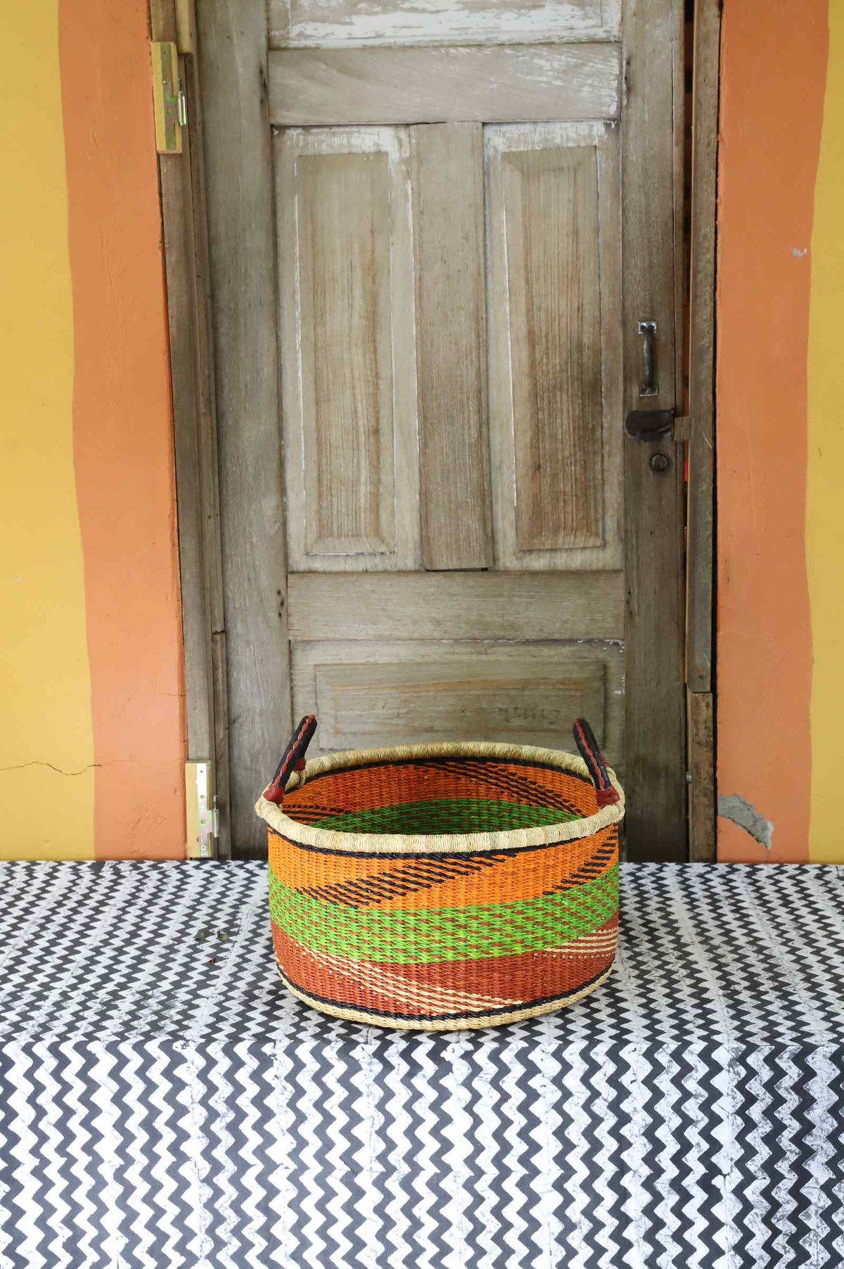 Small handwoven Bolga storage tub in natural straw with fine orange and green banded stripes.