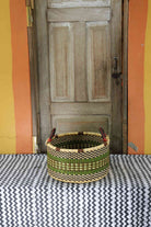 Small handwoven Bolga storage tub in dyed dark green with fine stripes and dark leather handles.