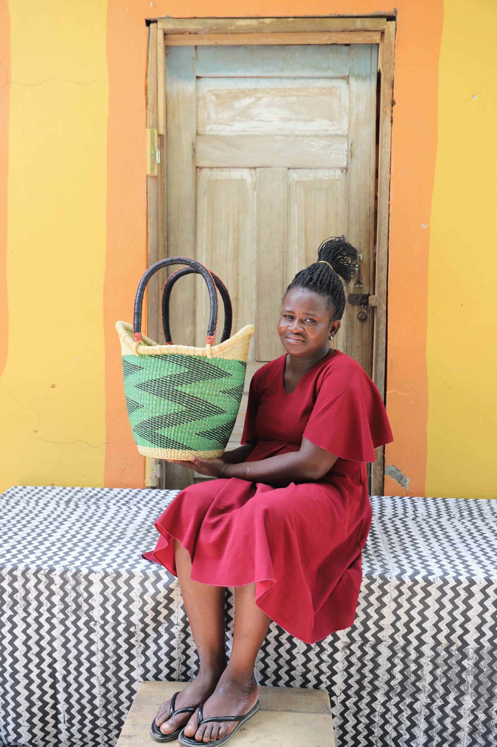 Medium Nyariga Bolga shopping basket in green with dark zigzag, held by a seated woman in red.