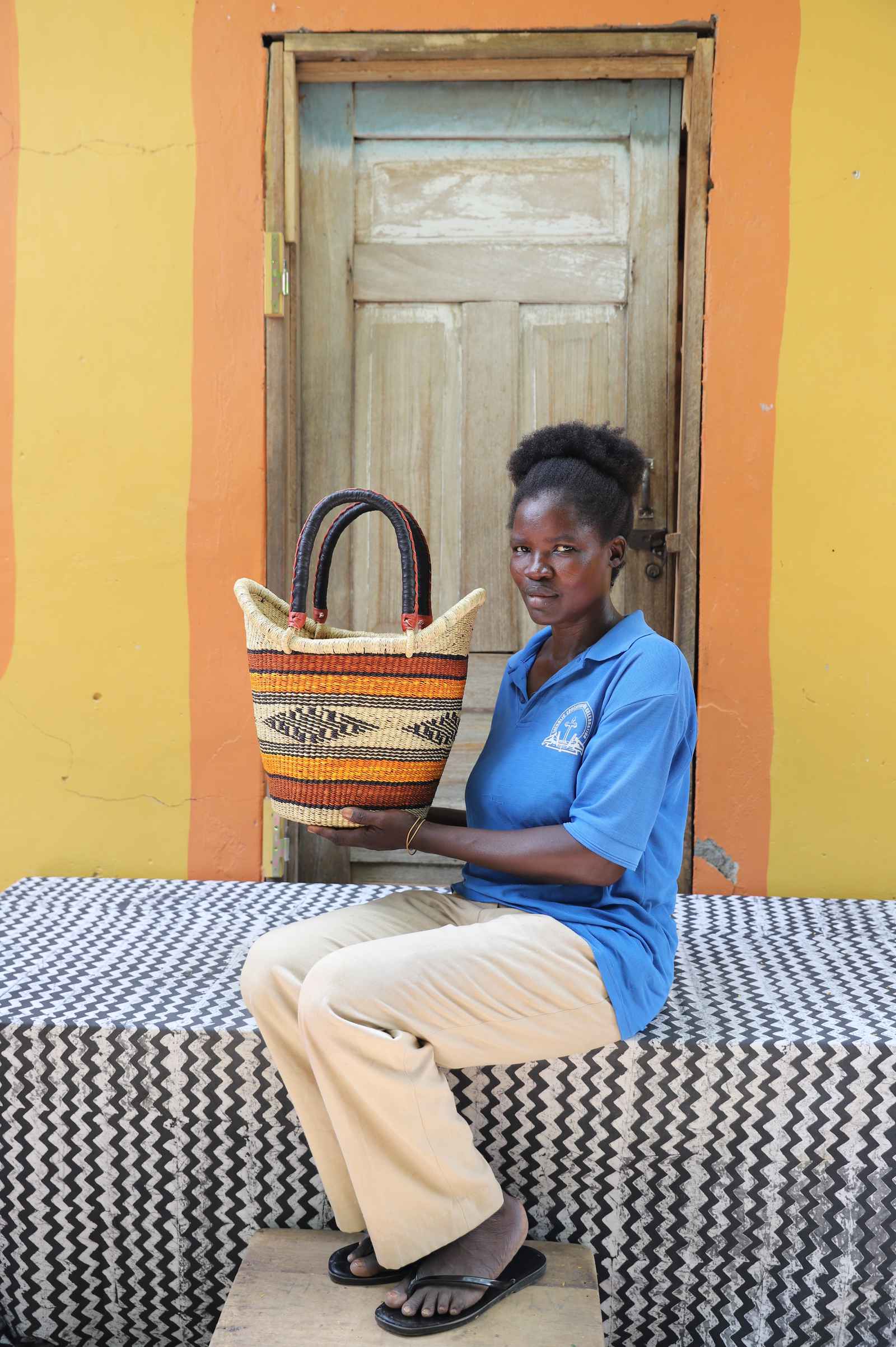 Small Nyariga Bolga shopping basket in orange and red stripes, held by a seated woman in blue.