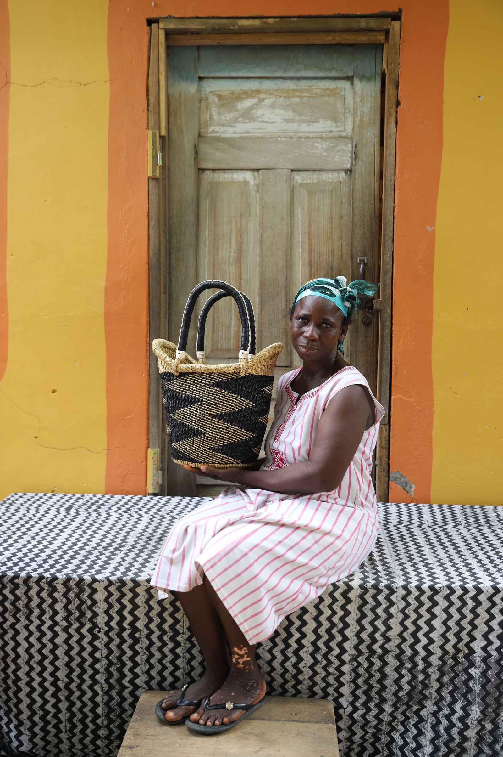 Small Nyariga Bolga shopping basket in natural with black zigzag, held by a seated woman in pink.