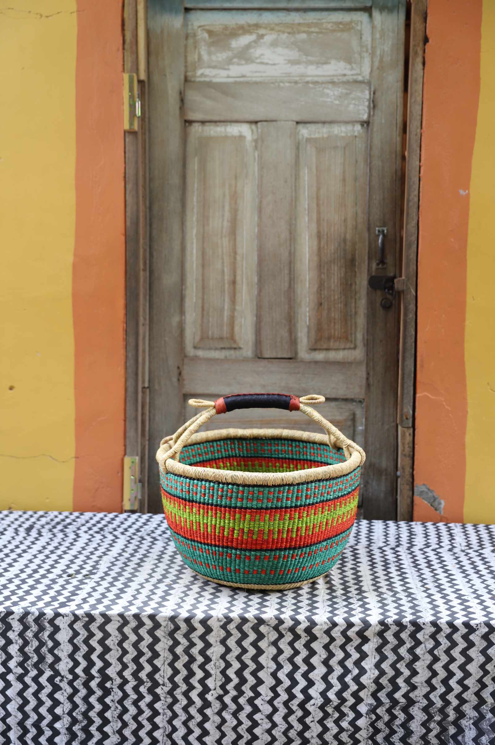 Large handwoven round Bolga shopping basket in natural straw with green, red and yellow banded stripes.