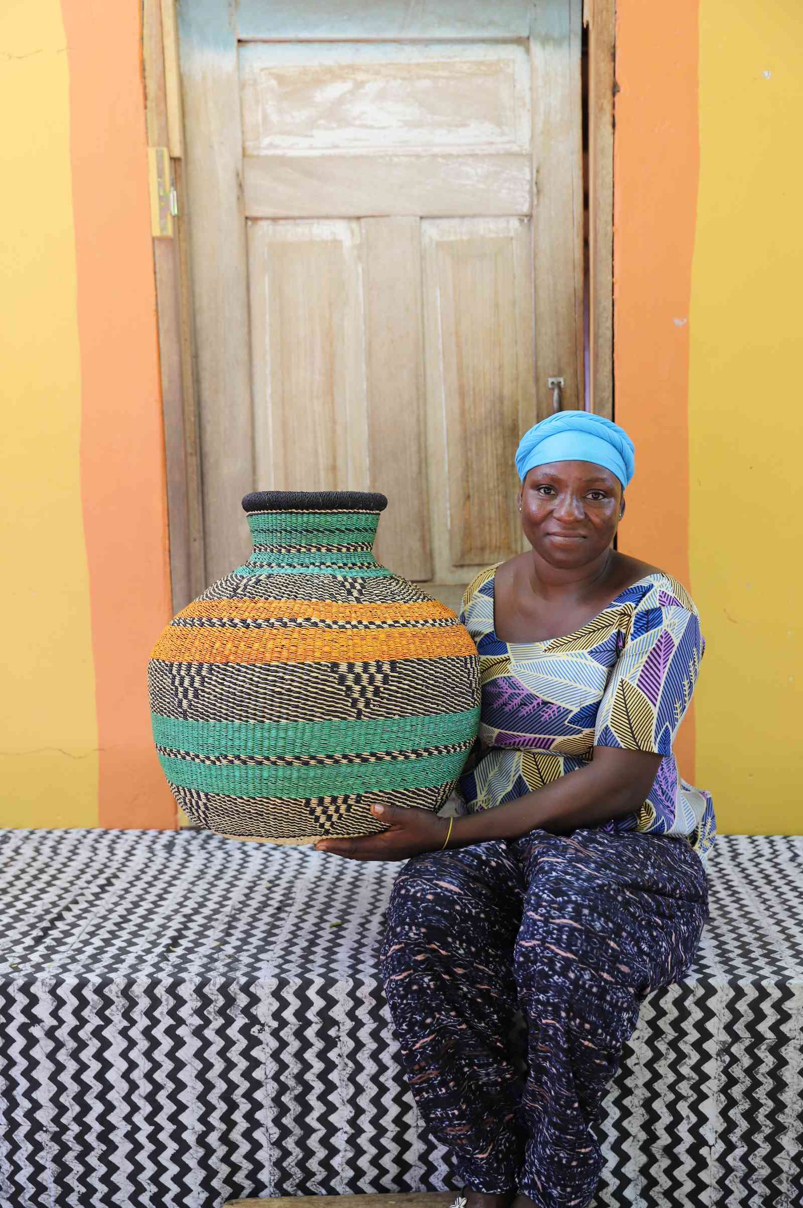 Large handwoven Bolga décor basket in orange and green bands, beside a seated woman.