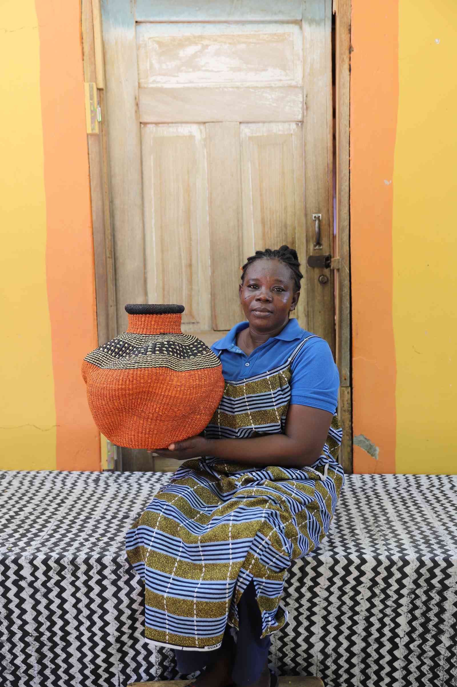 Handwoven Bolga art basket in rust-orange with a black and white shoulder, held by a seated woman in blue.