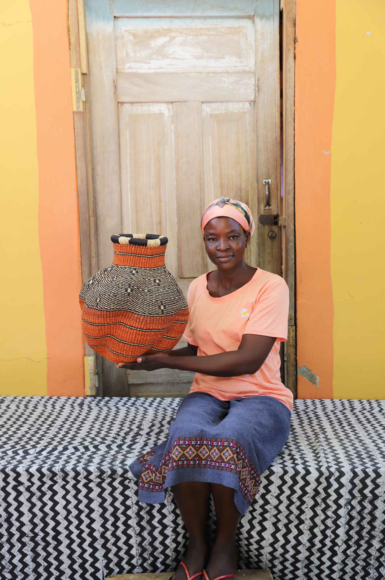 Handwoven Bolga art basket in rust-orange with a spotted shoulder, held by a seated woman in an orange top.