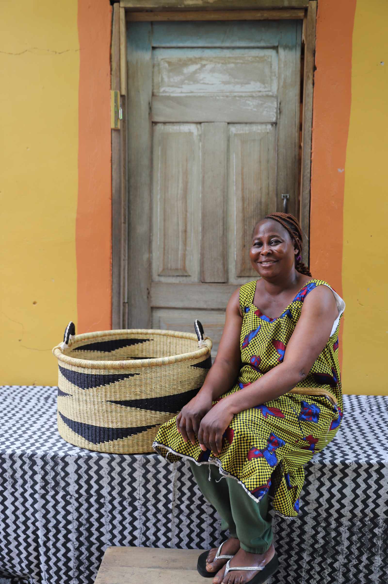 Large Bolga storage tub in dyed bold orange, beside a seated man in a striped tunic.