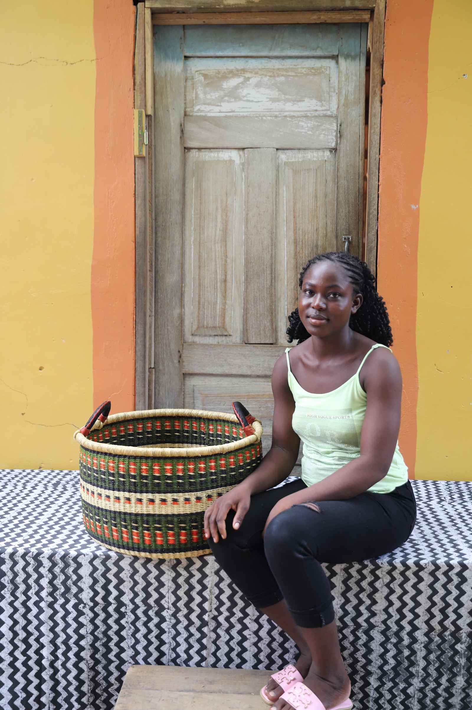 Medium Bolga storage tub in natural with dark zigzag triangles, beside a seated woman in yellow.