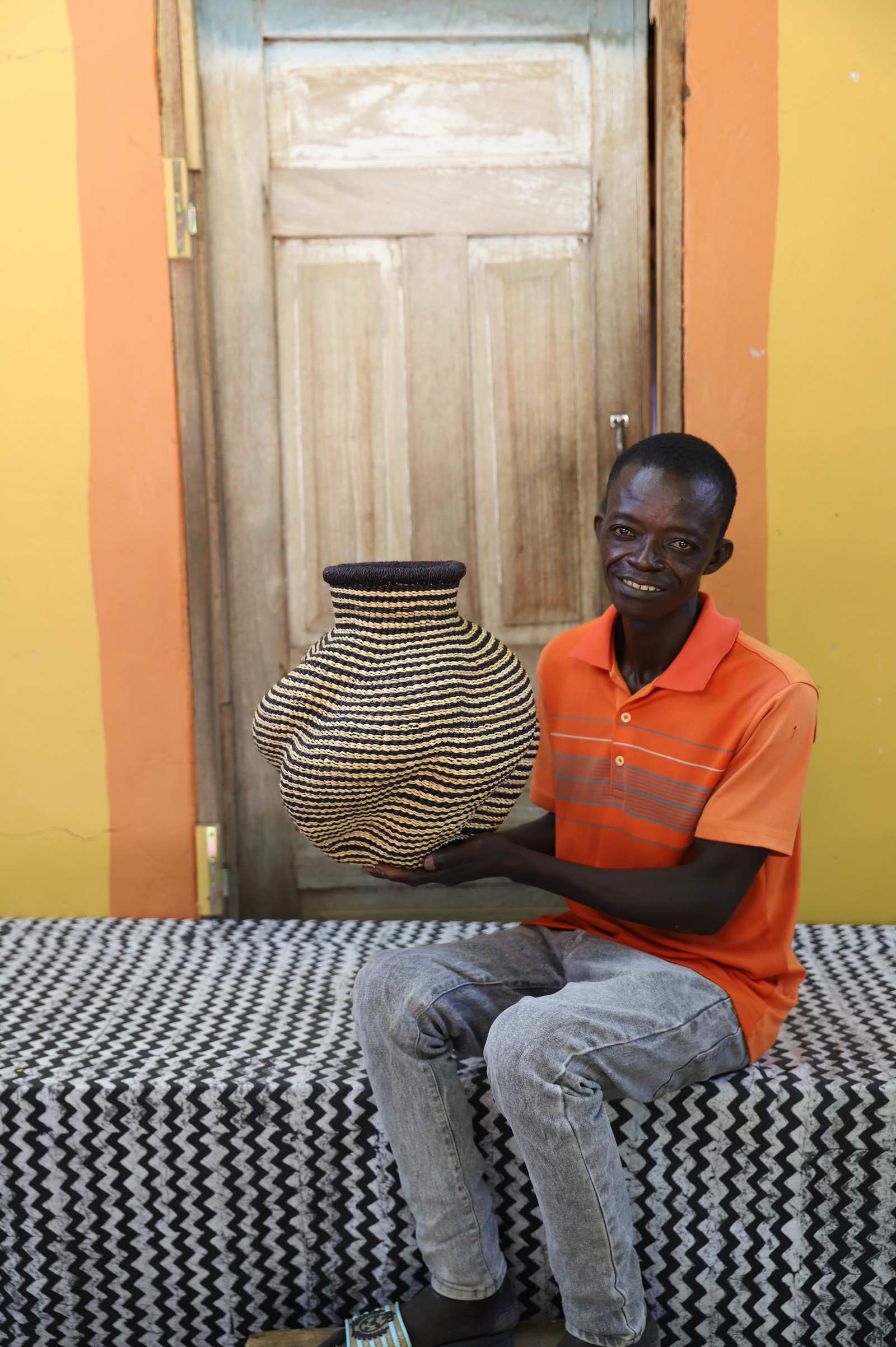 Handwoven Bolga art basket in natural straw with a fine diamond weave, held by a seated man in orange.