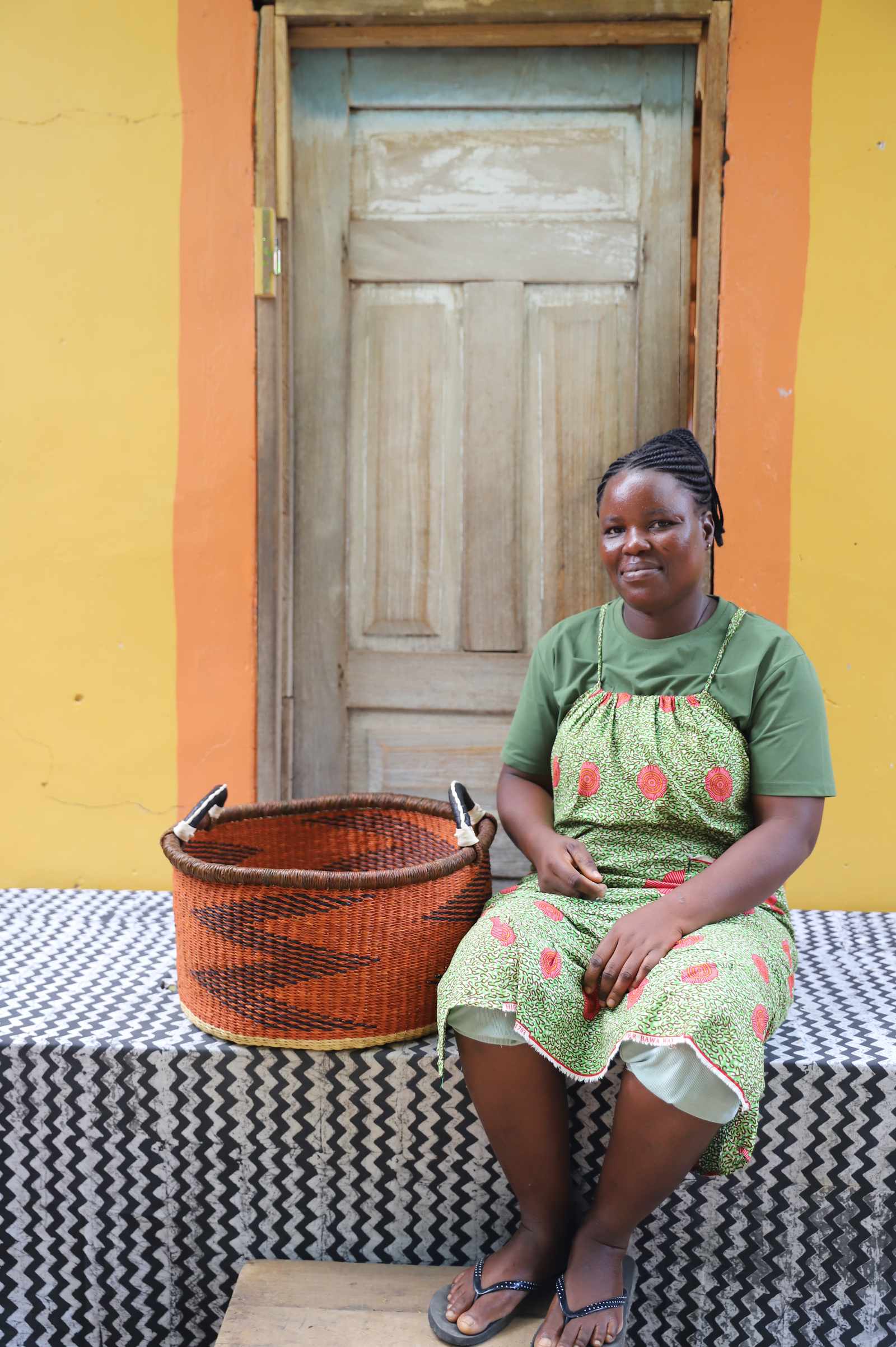 Small Bolga storage tub in dyed bold orange, beside a seated man in a white vest.