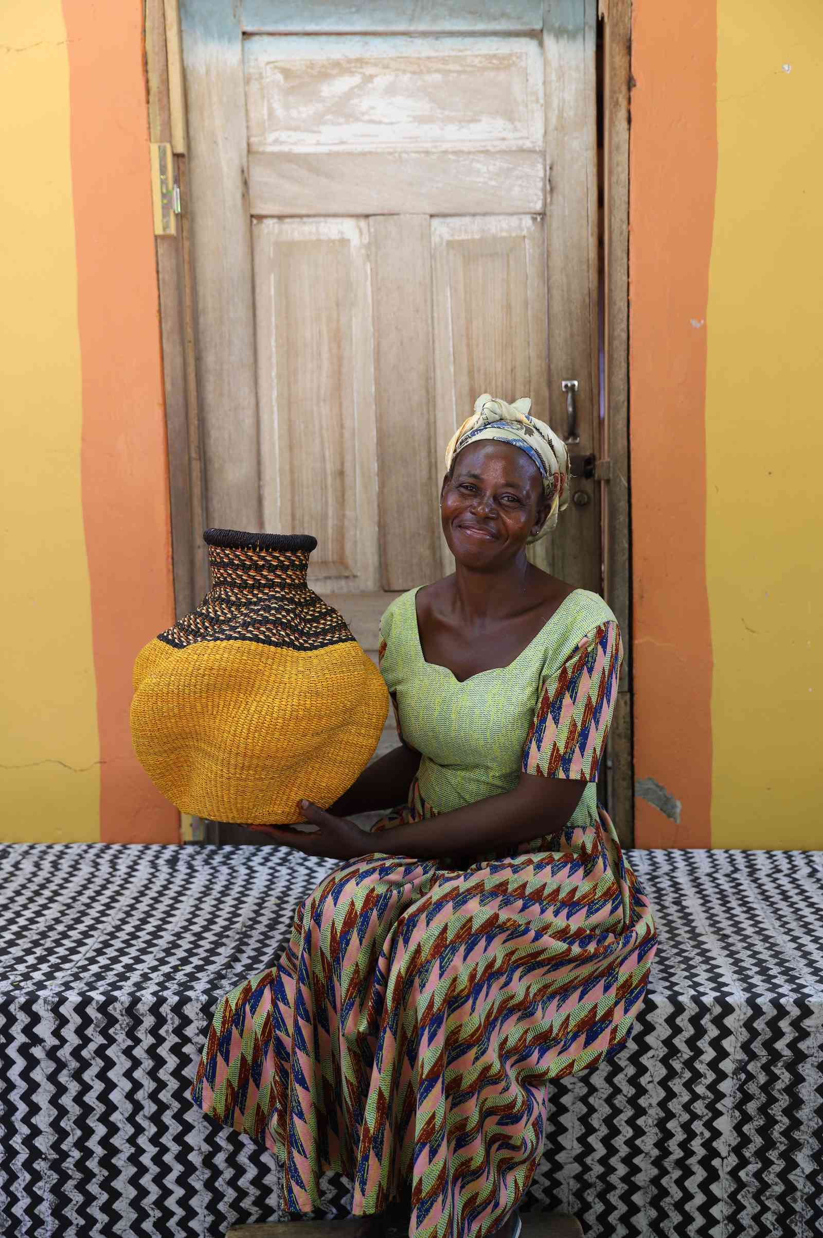 Handwoven Bolga art basket in mustard yellow with a dark zigzag shoulder, held by a seated woman in green.