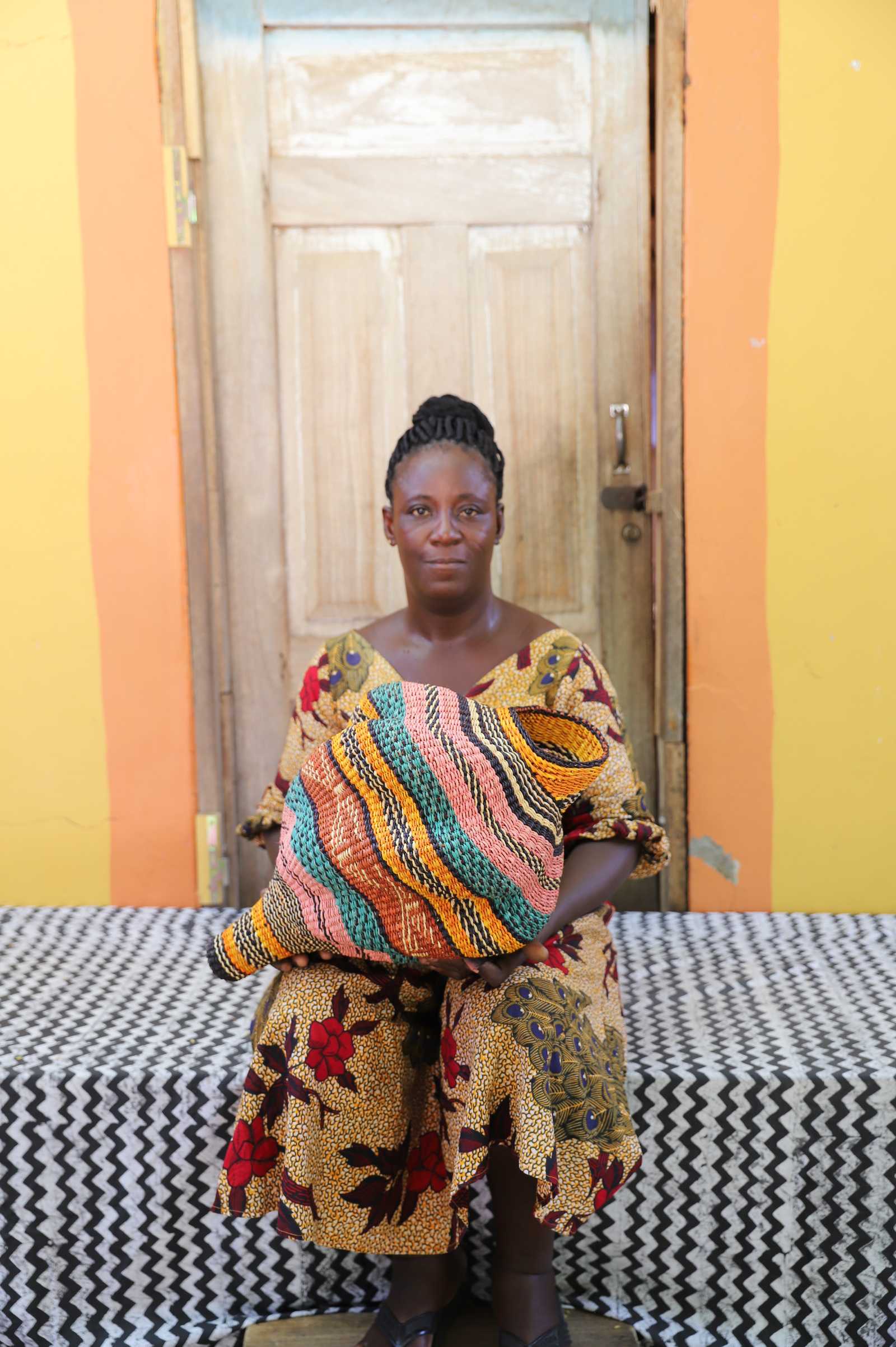 Handwoven Bolga art basket in a conch-shell form with multicolour stripes, held by a seated woman.
