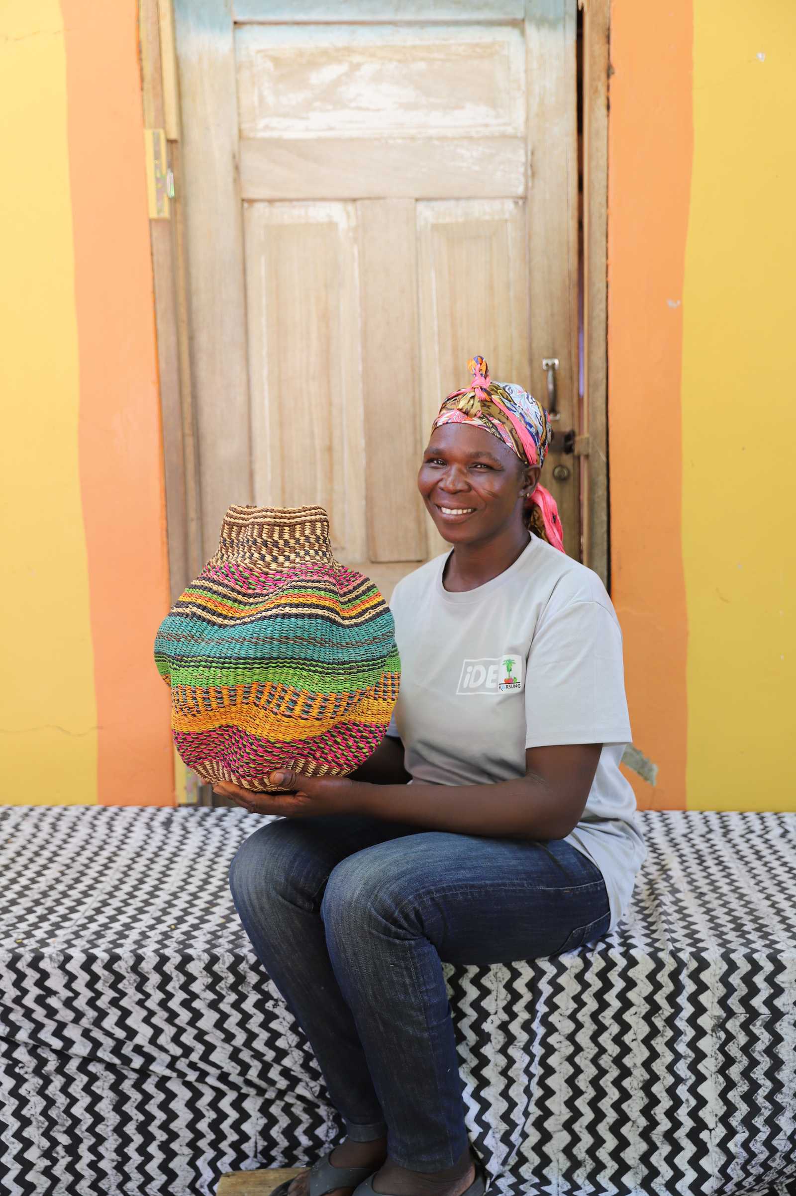Handwoven Bolga art basket in red, green and orange stripes, held by a seated woman in white.