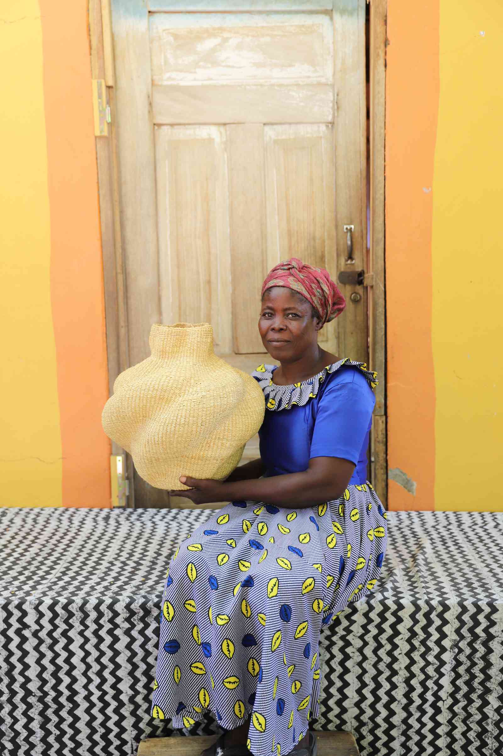 Handwoven Bolga art basket in a lobed natural straw form, held by a seated woman in blue.