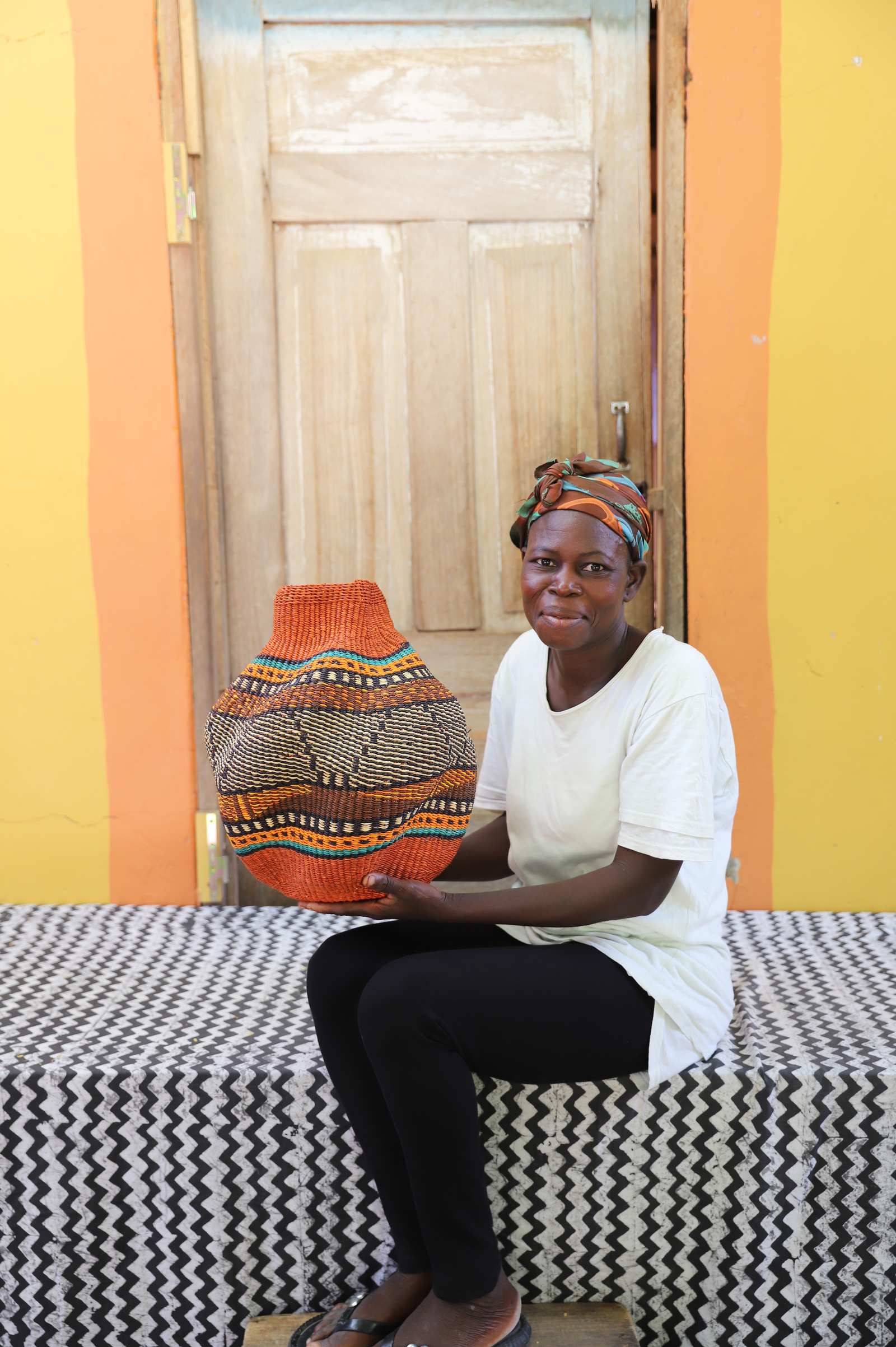 Handwoven Bolga art basket with orange rim and dark diamond weave, held by a seated woman in white.