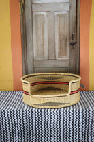 Large handwoven Bolga pet bed in natural straw with fine red horizontal stripes.