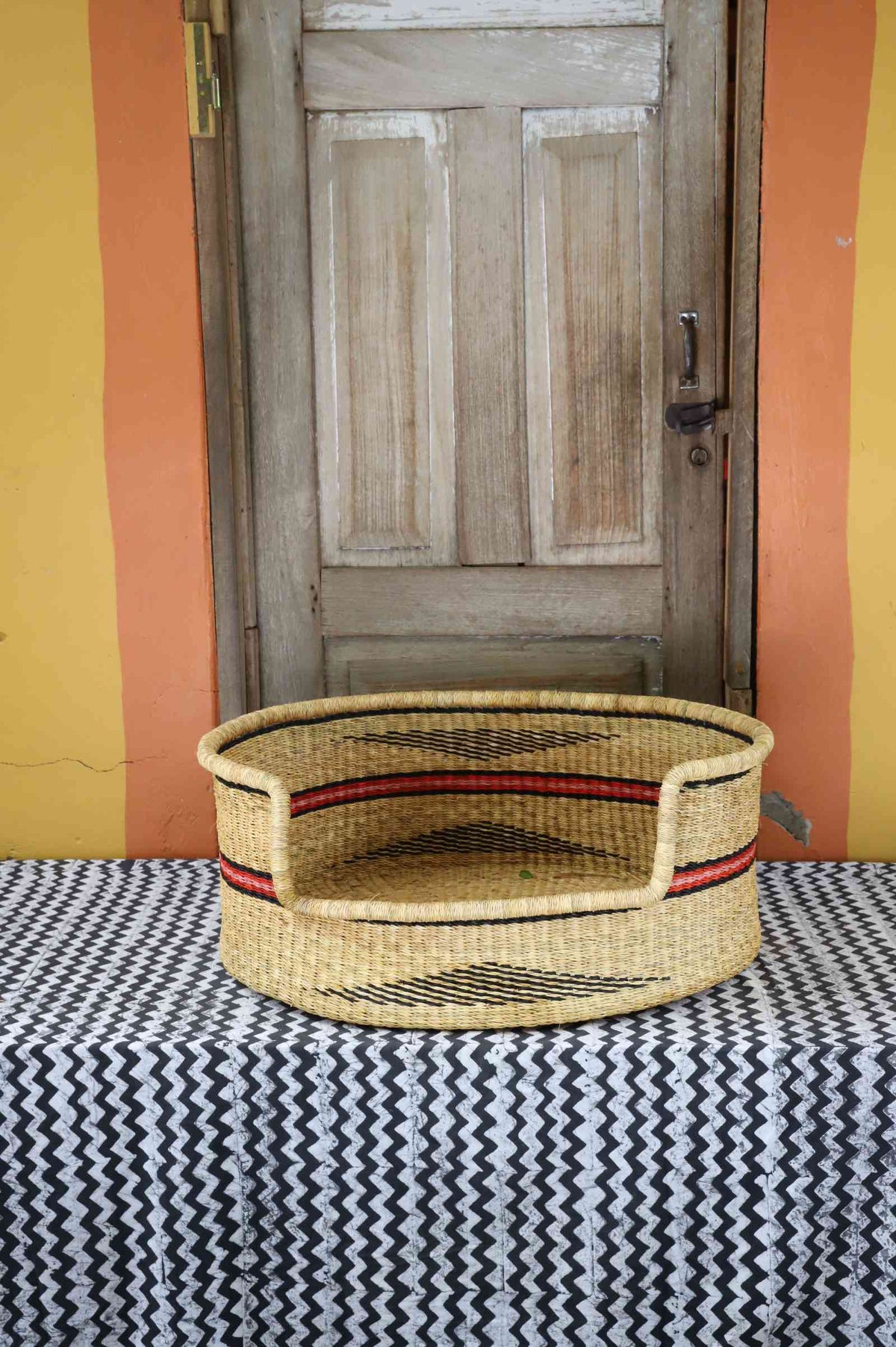 Large handwoven Bolga pet bed in natural straw with fine red horizontal stripes.