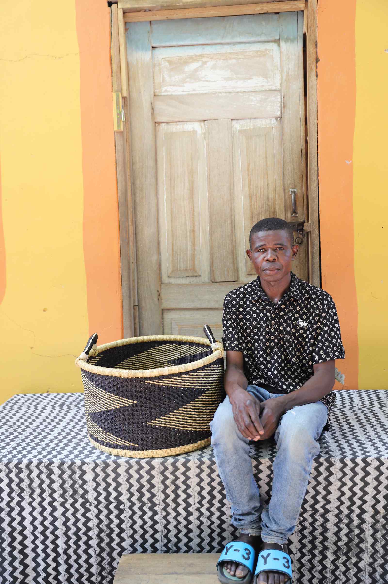 Medium handwoven Bolga storage tub in natural with dark zigzag pattern, beside a seated woman.